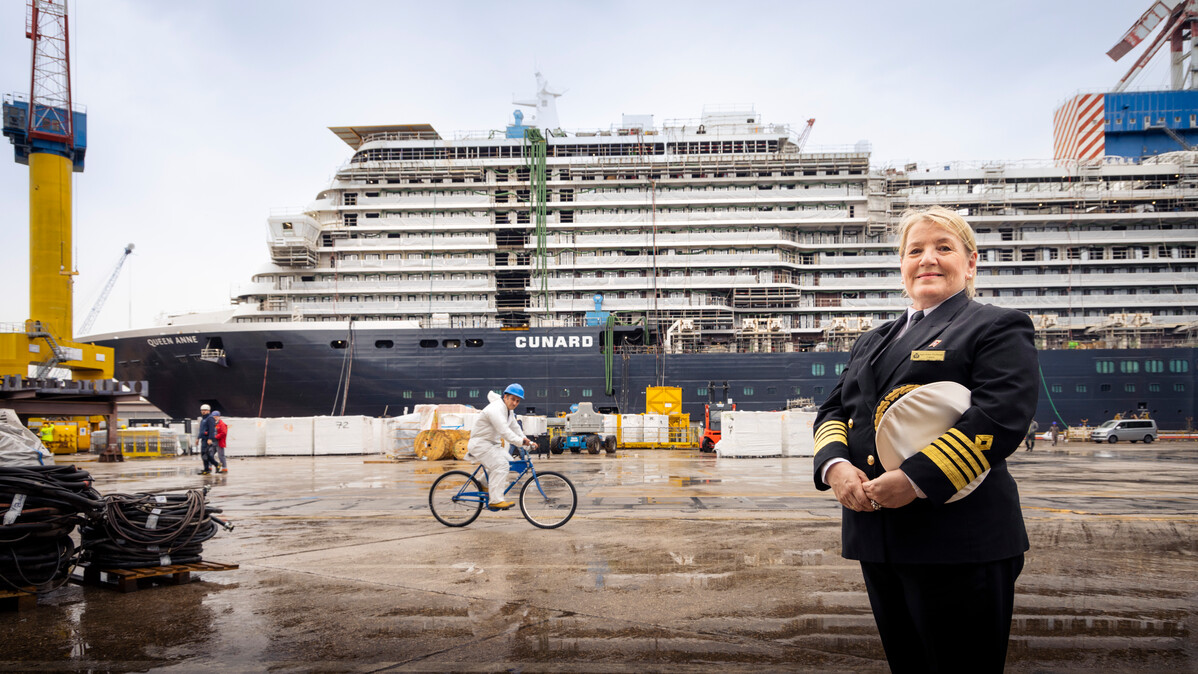 Captain Inger Klein Thorhauge standing in front of the Queen Anne cruise ship at a shipyard.